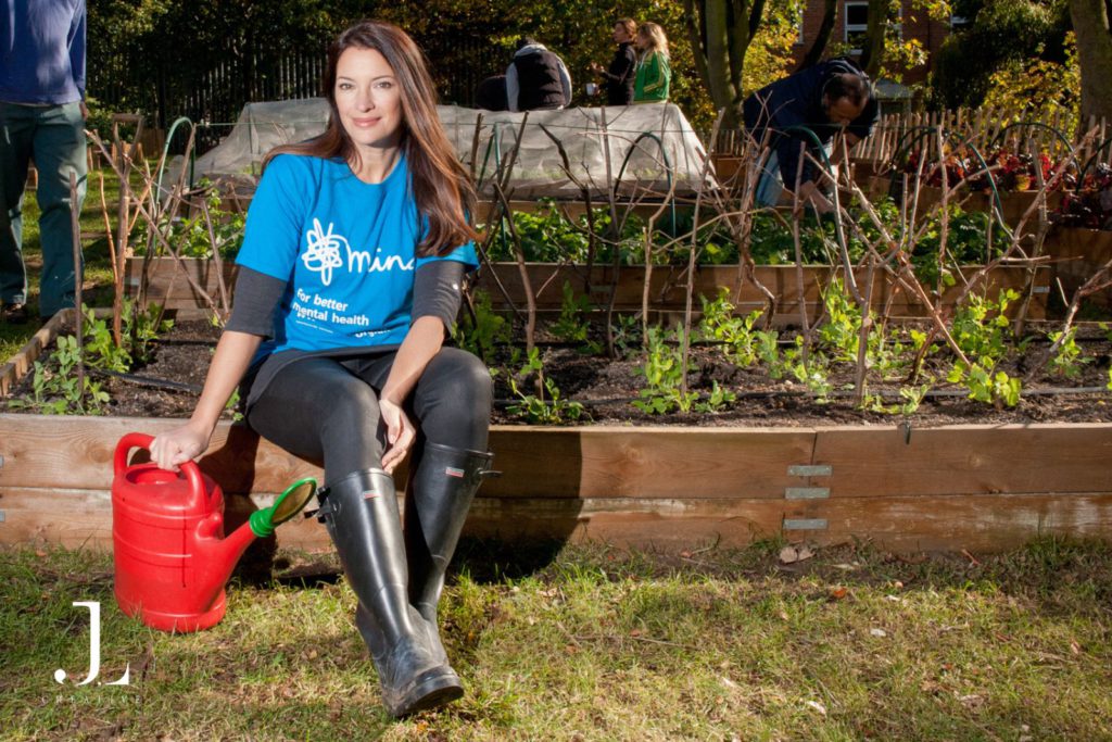 Rachel de Thame wearing a Mind charity t-shirt and wellies, sitting by a raised garden bed in Camden.
