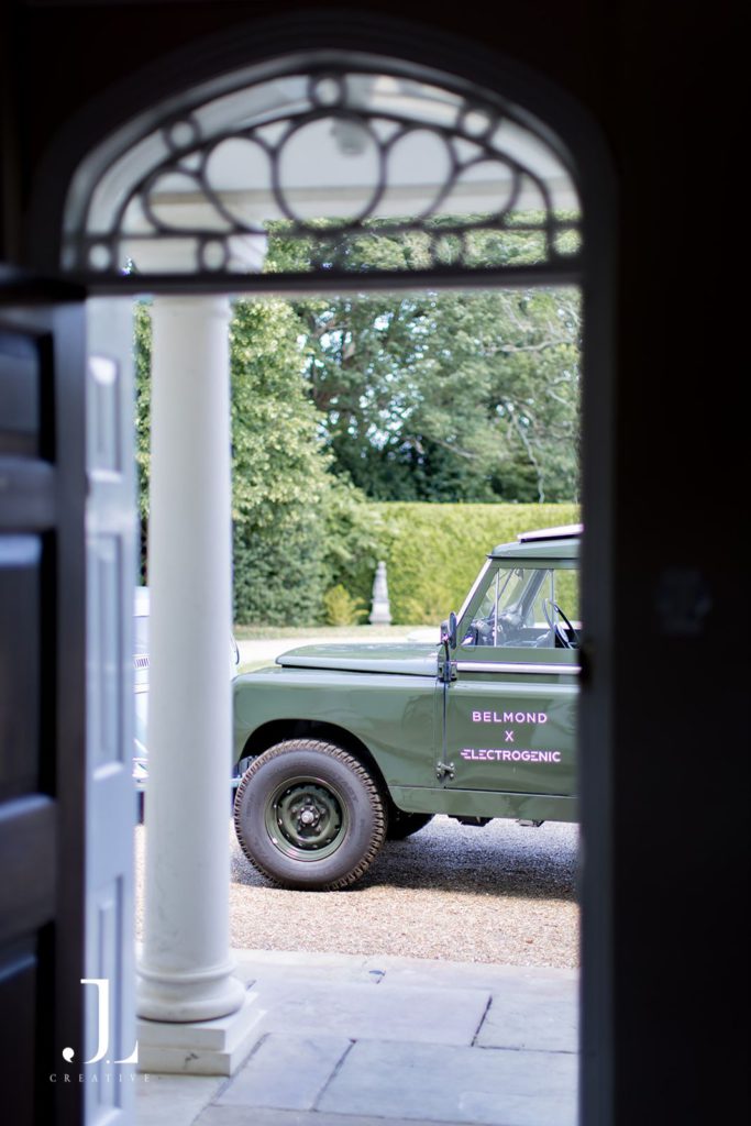 Side profile of a classic electric Land Rover with Belmond branding viewed through a doorway arch