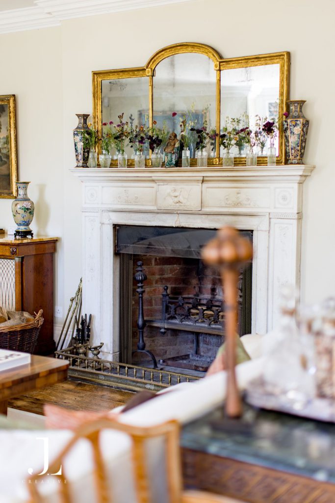 Ornate white fireplace and gilded triptych mirror with wildflower details in an estate interior