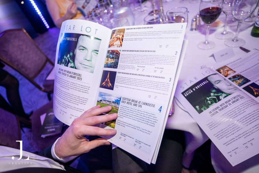 Close-up of a guest reading a TechUK annual dinner auction brochure