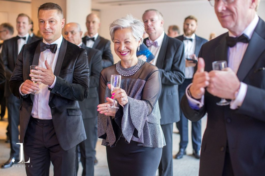 Smiling female guest with champagne and men in black tie.