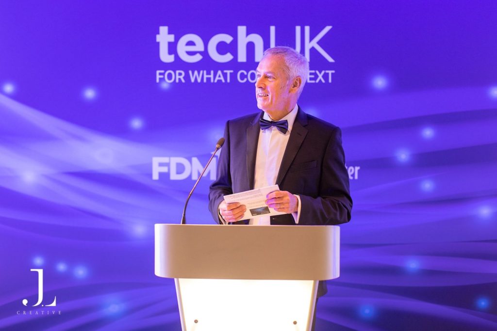 Host at a podium with TechUK branding and purple background
