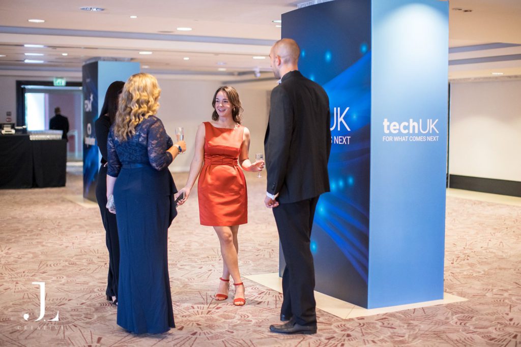 Guests in formal wear networking beside TechUK branded signage