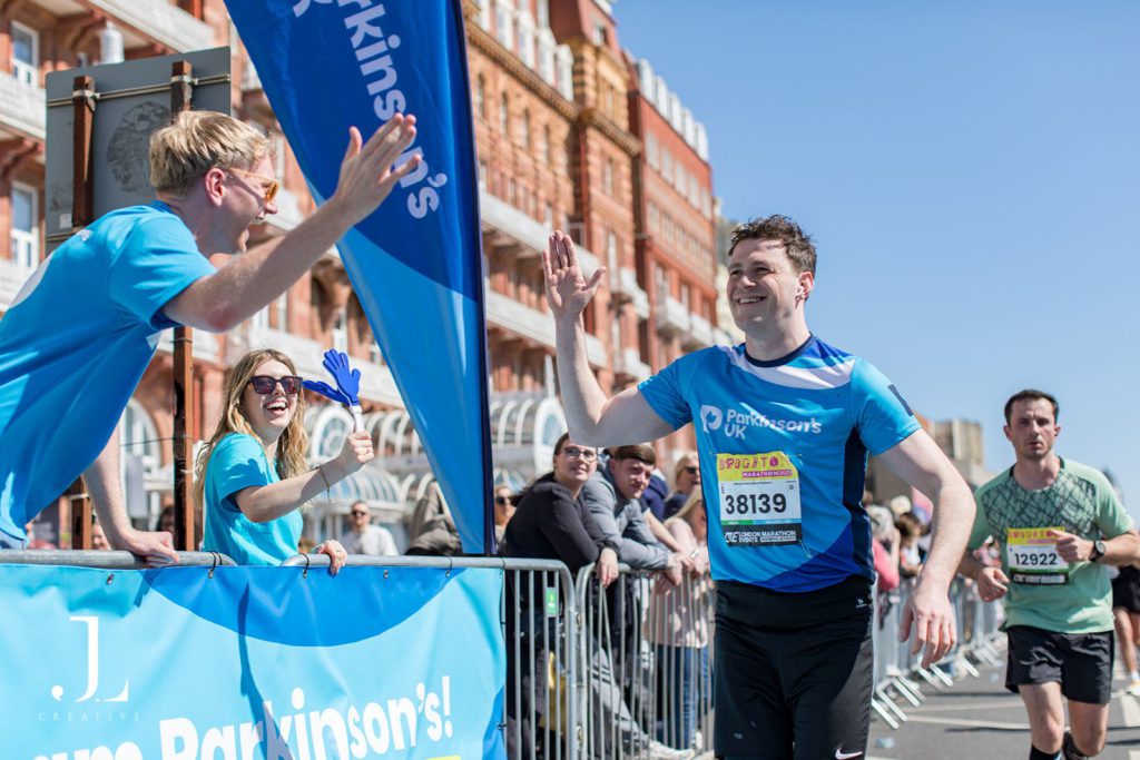 Runner high-fiving supporters at charity cheer point London Marathon