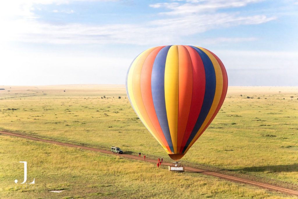 Luxury travel photography of a vibrant hot air balloon prepararing for takeoff over the vast Maasai Mara.