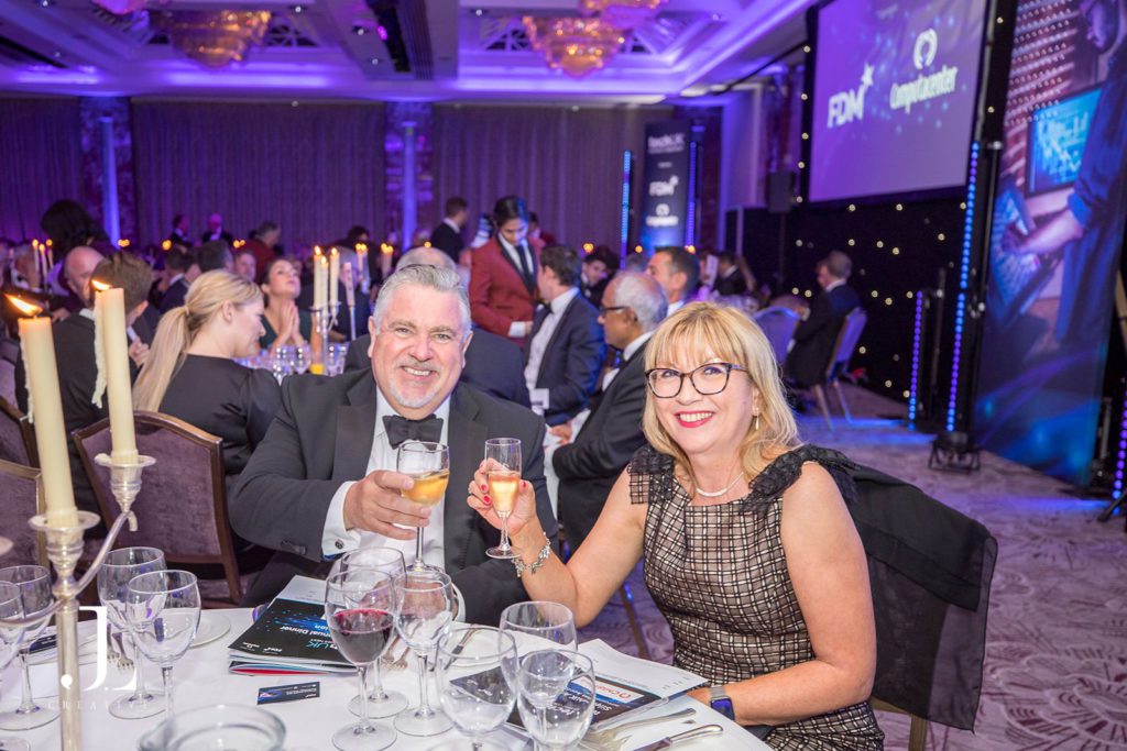 High-end event photography of a couple smiling and clinking glasses during a formal dinner celebration.