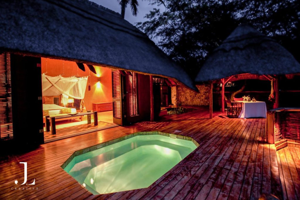 Luxury retreat photography of a private villa at night featuring a lit pool and elegant thatched-roof design.