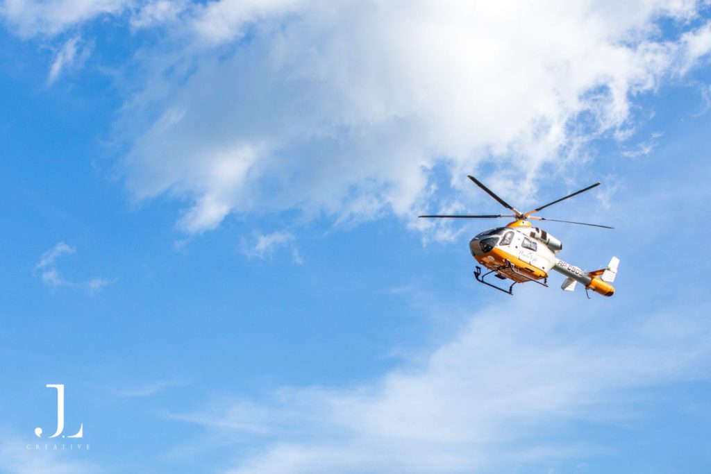 Experiential travel photography of a private helicopter soaring through a clear blue sky during a luxury retreat.