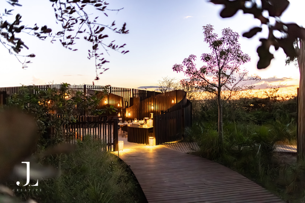 Wooden walkway leading to illuminated boma at sunset, part of luxury safari lodge photography in Botswana.