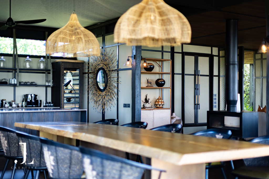 Long wooden dining table and woven pendants in lodge interior, shot for luxury hotel PR photography in Botswana.